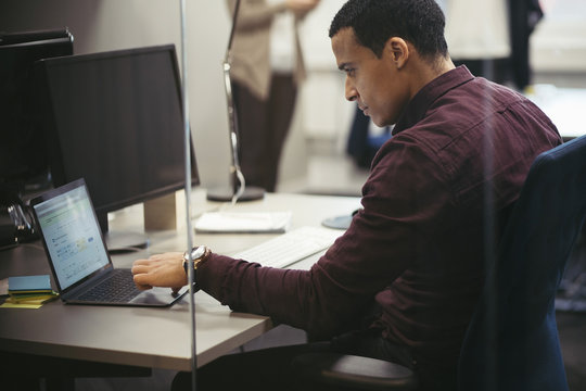 Businessman using laptop at desk in office with colleague in background