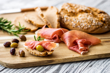 Prosciutto with olives on wooden background