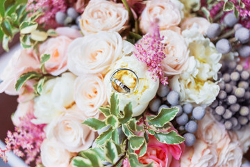 Golden wedding rings with diamonds lie inside rose flower in the bridal bouquet. Symbol of love and marriage.
