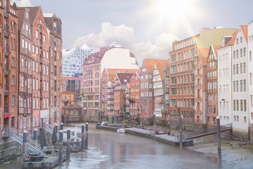 historic buildings on both sides of Nikolaifleet channel in Hamburg, Germany with Elbphilharmonie concert hall in background under blue summer sky