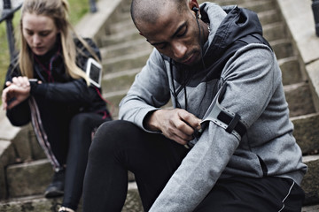 Mid adult man wearing smart phone on arm while woman checking time in background on steps