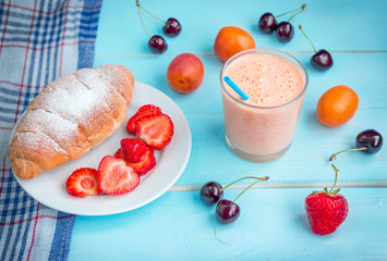 Served breakfast or snack. Apricot  smoothie in a glass with straw, croissant, ripe and juicy strawberry and cherries. Summer fruits and berries and pastry.