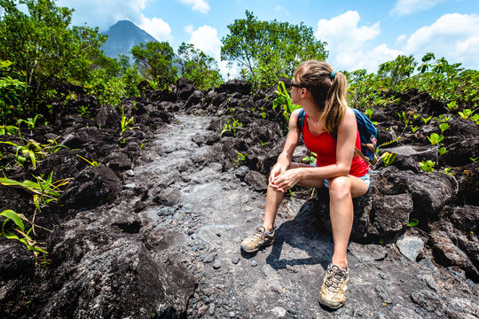 Young woman hiker relaxing on the hard and rocky lava trail with volcano on the horizon