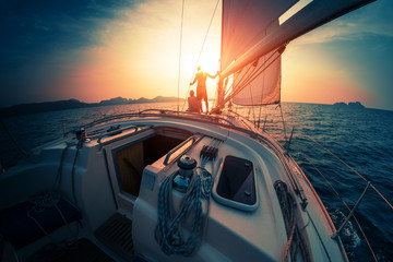 Young couple enjoys sunset from the sailing boat moving in the tropical sea