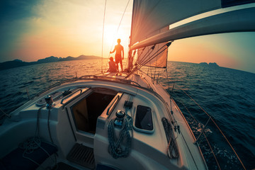 Young couple enjoys sunset from the sailing boat moving in the tropical sea - obrazy, fototapety, plakaty