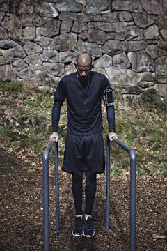 Full length of male athlete exercising on parallel bars in forest