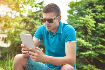 Young man using tablet on park bench on a summers day
