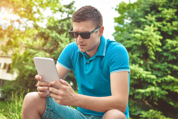 Fototapeta premium Young man using tablet on park bench on a summers day