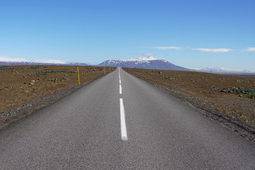 Long asphalt road F35 in the central Iceland between brown fields and in front of high Icelandic mountains