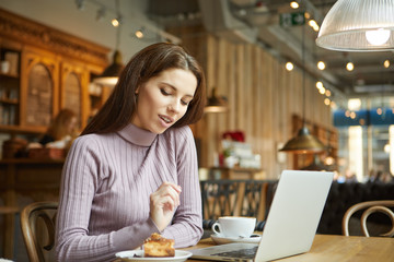 Fototapeta na wymiar Beautiful brunette using laptop in cafe. Blogger work concept