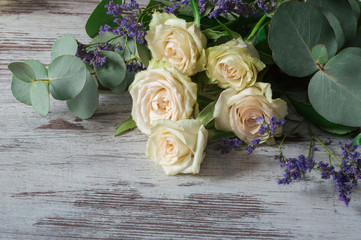 White fragrant roses with some branches of eucalyptus on gray background.