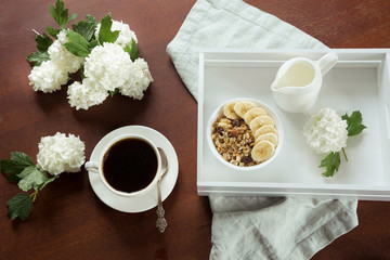 A healthy breakfast from a cup of black coffee,  muesli, sliced bananas and decor with flowers of viburnum. View from above.