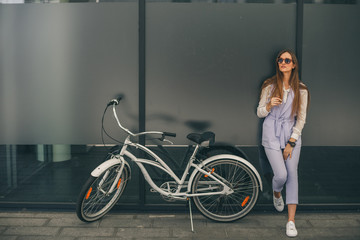Plakat Beauty with vintage bike. Beautiful young smiling woman standing near her vintage bicycle while she leans against the wall.