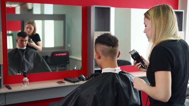 The blonde hairdresser cuts her hair with an electric razor, a man who came to a beauty salon and sits in front of a mirror expects a change of image and good service