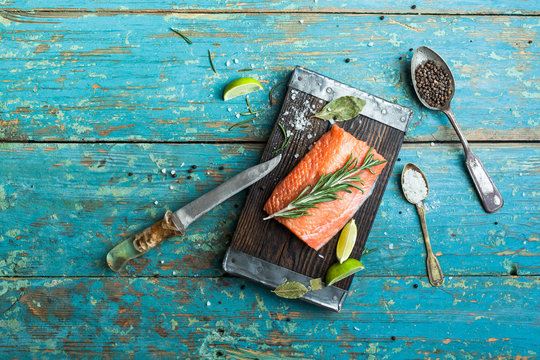 A piece of raw salmon, spices, knife, board, spoon, lime on the old shabby blue table, top view. Preparation for cooking fish food. Salmon steak.