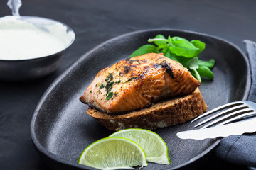 Fish steak in a frying pan with basil close-up, fork and knife, sauce on a dark metallic background. Fish meal.