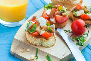 Bruschetta with tomato, bacon, matsarela and parsley on a wooden plate, a cup of orange juice on a blue tablecloth. Close-up. Italian appetizer.