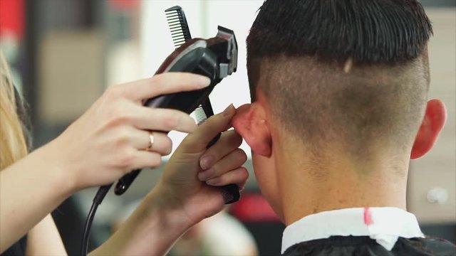 The modern stylist cuts her hair with a shaving machine and scissors, the woman neatly changes the length of the hair of a visitor to the barbershop