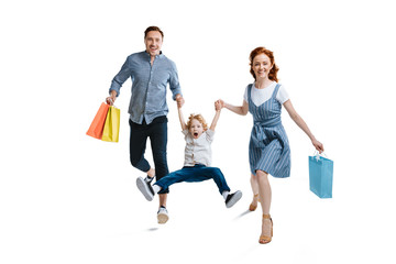 Happy young family with one child holding shopping bags and smiling at camera isolated on white