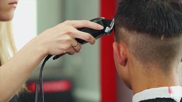 Close up shot of the barber's hands, who cuts the hair of the man on his head, the hair stylist uses an electric hair machine to change the length of the hair behind