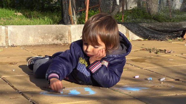 4K Kid borely draws with chacks lying on concrete slabs