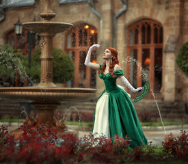 A beautiful red-haired girl in a ball gown is walking by the fountains.