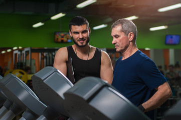Senior man working with personal trainer in gym.