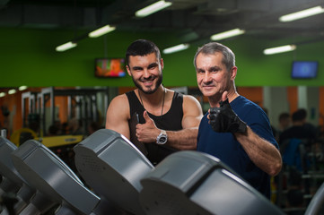 Fototapeta na wymiar Senior man working on treadmill with trainer