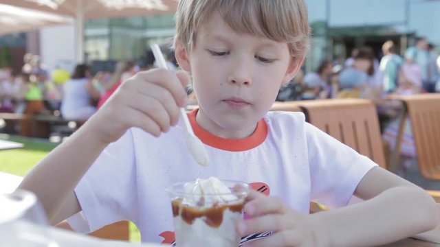 The boy is eating ice cream. Blonde boy eating ice cream looking at camera.