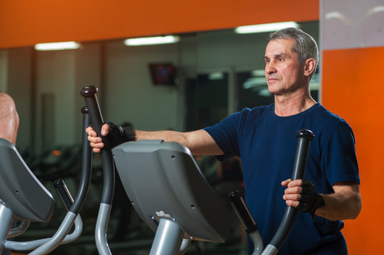 Senior Man Exercising On Elliptical Machine In Gym