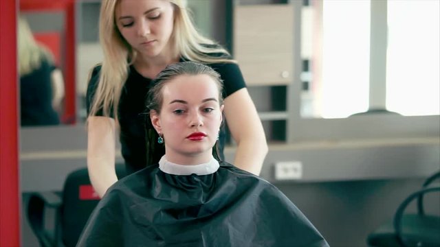 A young and experienced hair stylist who goes through the practice in a beauty salon combs his wet hair in order to dry his hair with a hairdryer and make stylish curls.