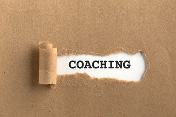 The text COACHING behind torn brown paper