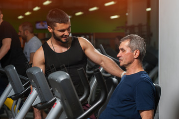 Fototapeta na wymiar Senior man working with personal trainer in gym.