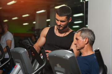 Fototapeta na wymiar Senior man working with personal trainer in gym