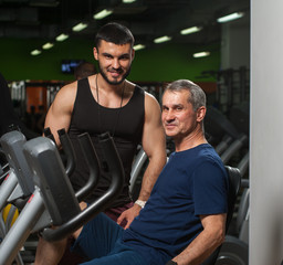Fototapeta na wymiar Senior man exercising with trainer in gym