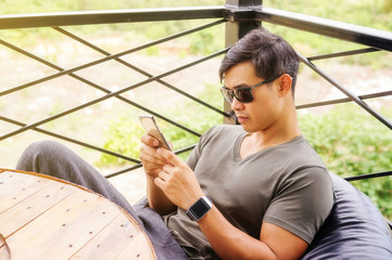Asian young man wears a sunglasses and uses a smartphone.