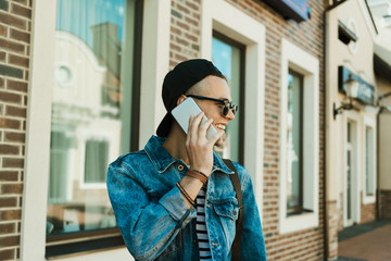 Smiling young man in cap and sunglasses talking on smartphone and looking away