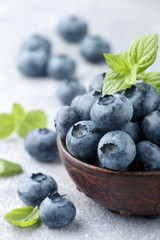 Fresh organic blueberries in a clay bowl. Juicy berry and mint leaves on a stone or concrete background. Natural antioxidant,  superfood. concept for healthy eating and nutrition