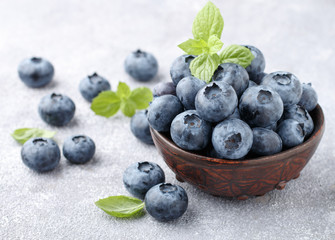 Fresh organic blueberries in a clay bowl. Juicy berry and mint leaves on a stone or concrete background. Natural antioxidant,  superfood. concept for healthy eating and nutrition