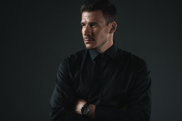 fashionable man in black outfit with crossed arms looking away, isolated on grey