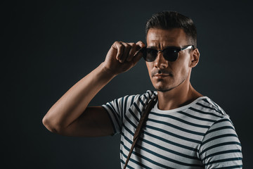 Obraz premium confident stylish man posing in striped t-shirt and sunglasses, isolated on grey