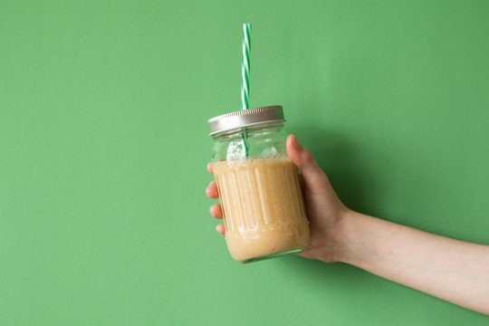 Woman hand holding smoothie shake against colored wall. Drinking yellow healthy smoothie concept.