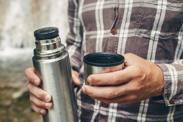 Unrecognizable hiker man pours tea or coffee from thermos Resting Hiking Concept