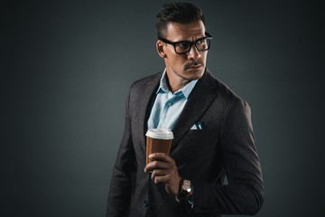 portrait of stylish man with coffee to go in hand looking away isolated on grey