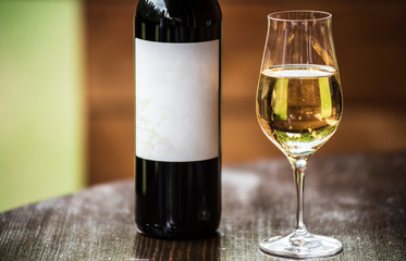 A glass with a white wine and the black wine bottle with label. Selective focus.