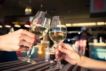 Young couple with glasses of white wine on a date in a cozy Italian restaurant. Leisure, drinks, people and holidays concept - happy man and woman clinking glasses.