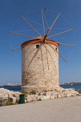 Fototapeta na wymiar Windmill Papagiorg whit Vati in Rhodes harbor. Old defensive stands and windmills. Wharf harbors, boats and sailing ships. Historic pier and beach.