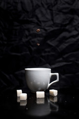 Fototapeta na wymiar A cup of fragrant coffee and a few slices of sugar next to a black background