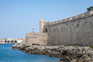Fototapeta na wymiar Harbor and monuments in Rhodes. Old defensive stands and windmills. Wharf harbors, boats and sailing ships. Historic harbor, pier and beach.