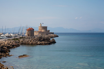 Harbor and monuments in Rhodes. Old defensive stands and windmills. Wharf harbors, boats and sailing ships. Historic harbor, pier and beach.